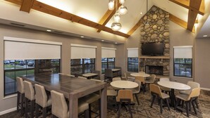 A spacious indoor area with a large wooden table and chairs, a stone fireplace, and a television mounted on the wall.