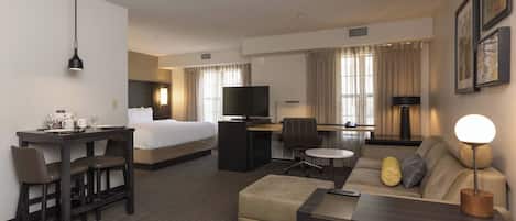 A hotel room with a bed, desk, sofa, and TV.