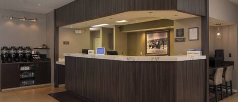 A reception area with a dark wood reception desk, a coffee station, and a seating area with chairs.