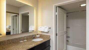 Une salle de bain avec un comptoir en granit, un lavabo, un miroir et une douche.