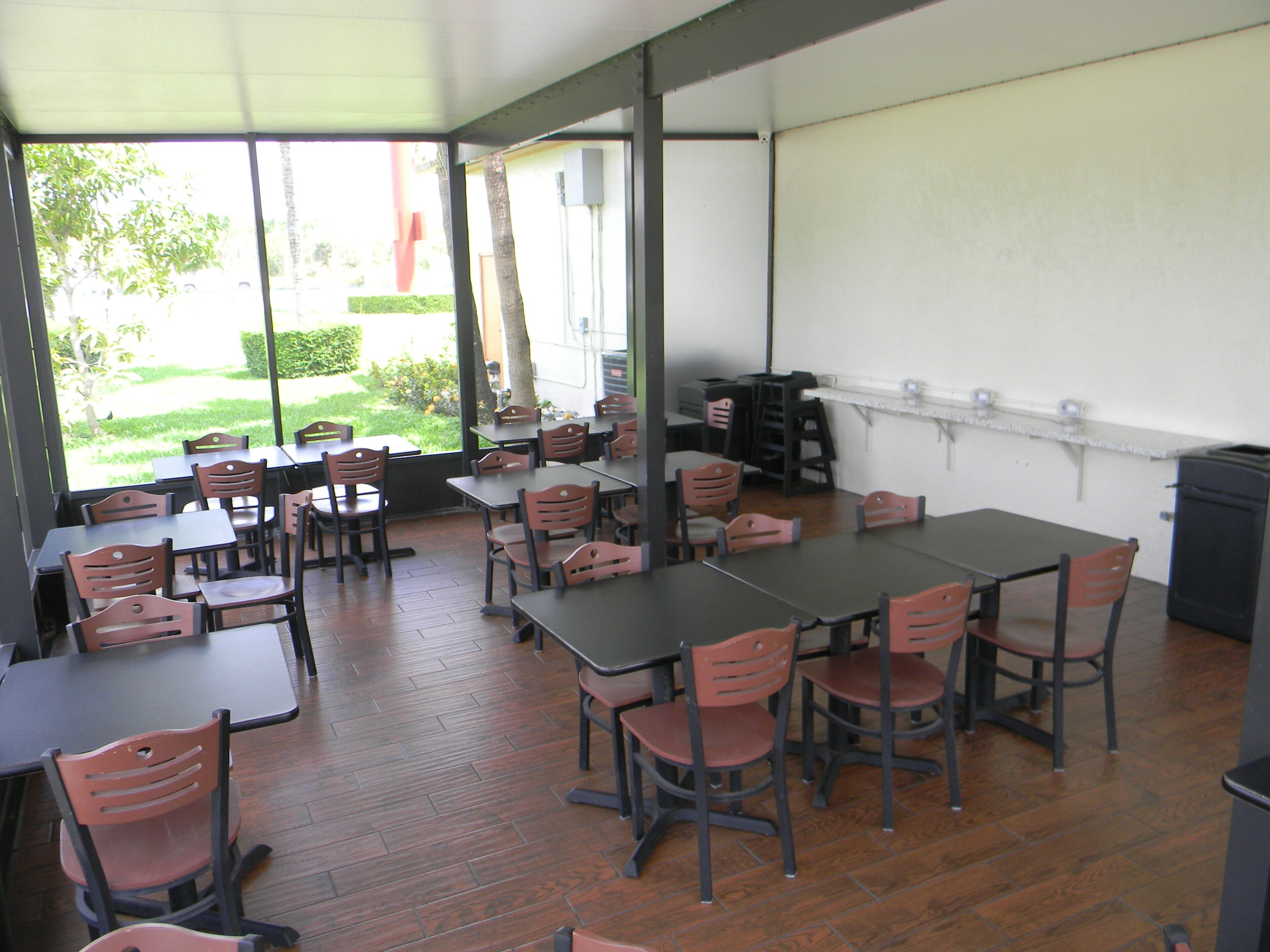 An indoor dining area with tables and chairs, large windows, and a view of greenery outside.
