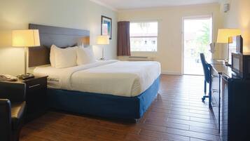 A hotel room with a large bed, bedside tables, a desk with a chair, a television, and a window with curtains.