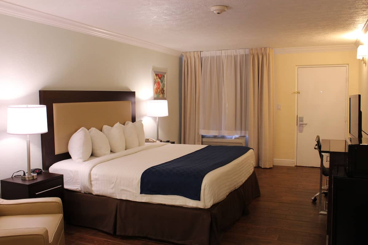 Une chambre d’hôtel avec un grand lit, deux lampes de chevet, un bureau avec une chaise, une télévision et une fenêtre avec des rideaux.