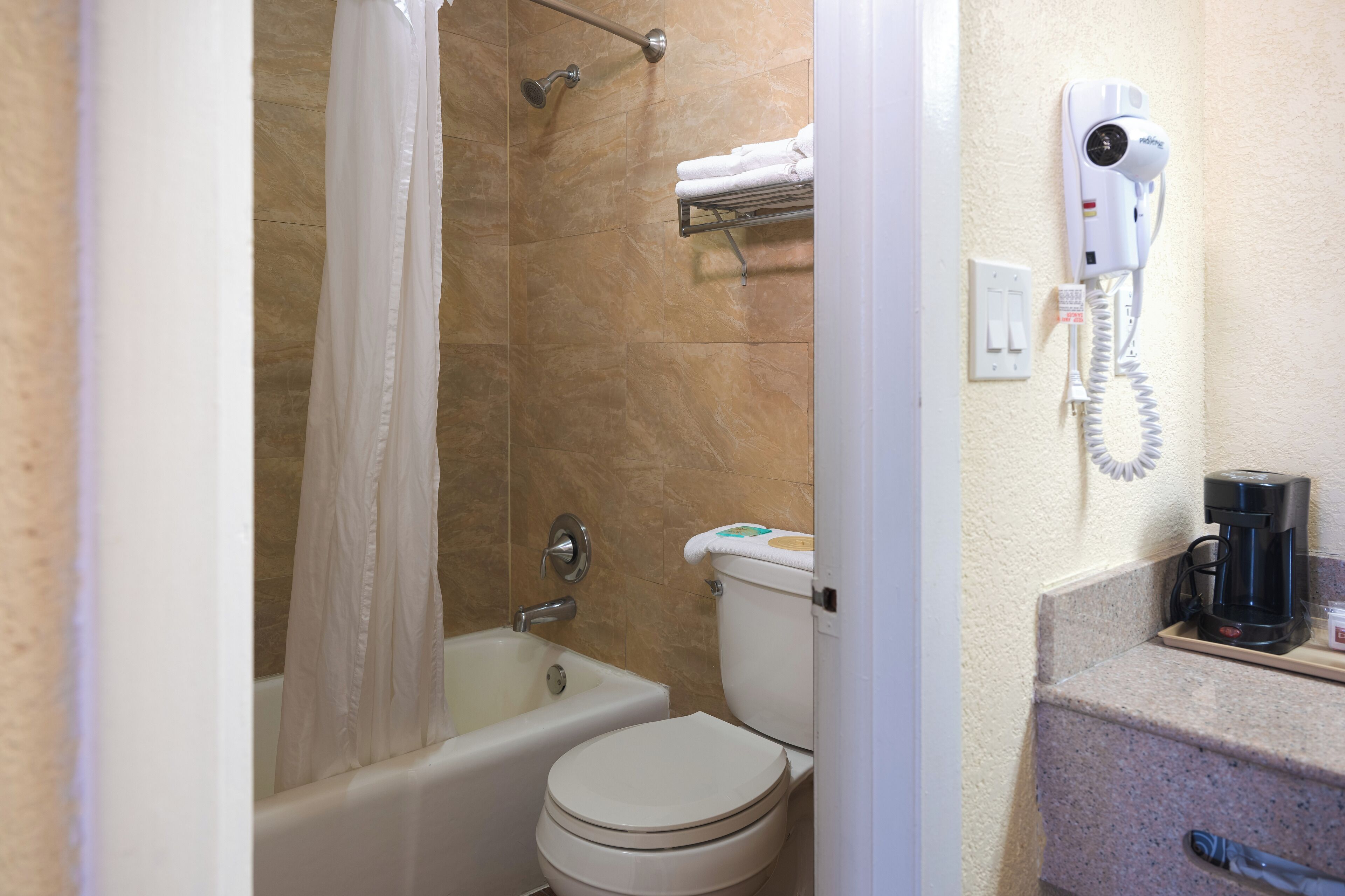 A bathroom with a bathtub, toilet, and a hairdryer mounted on the wall.
