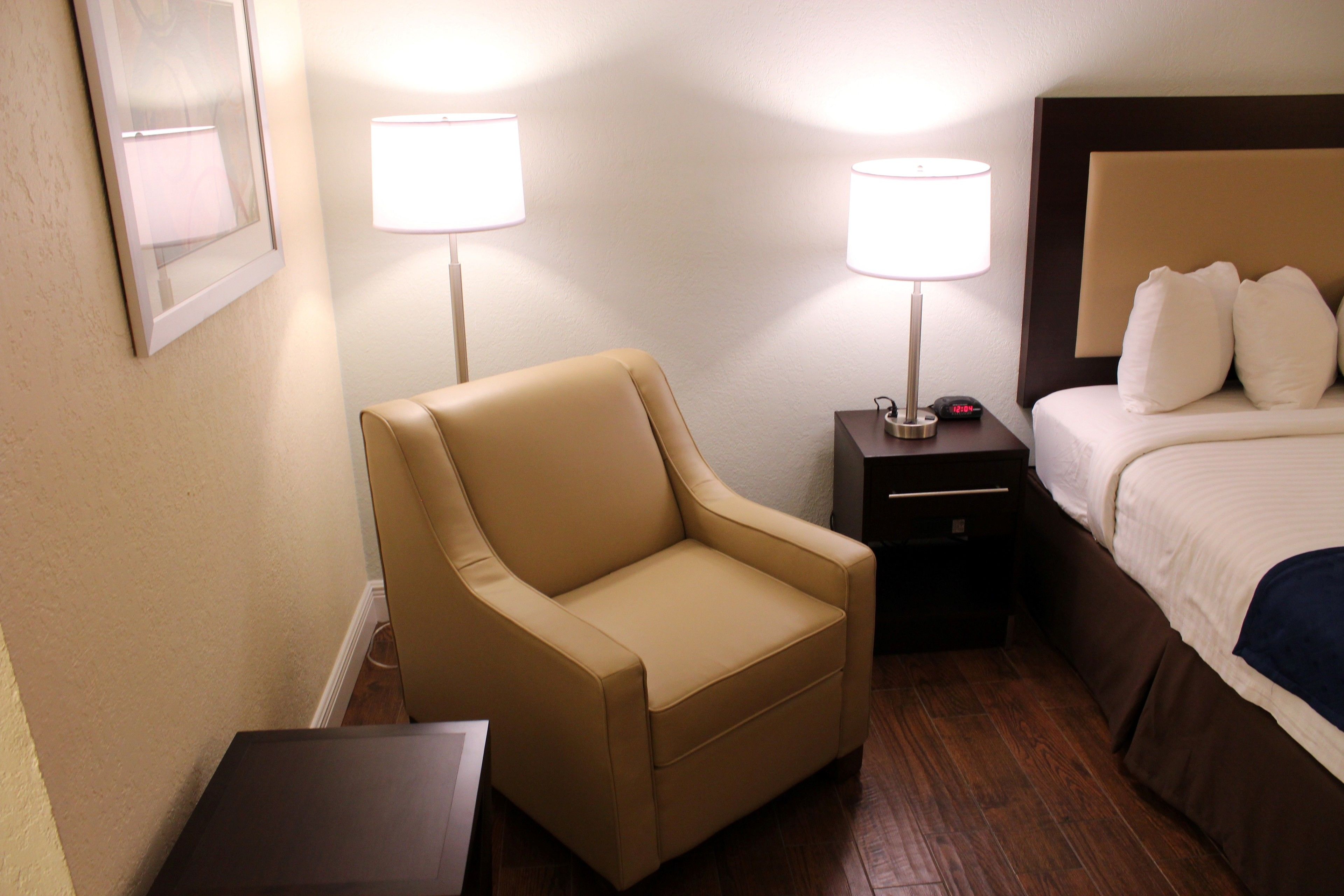 A hotel room with a bed, a chair, two bedside tables with lamps, and a framed picture on the wall.