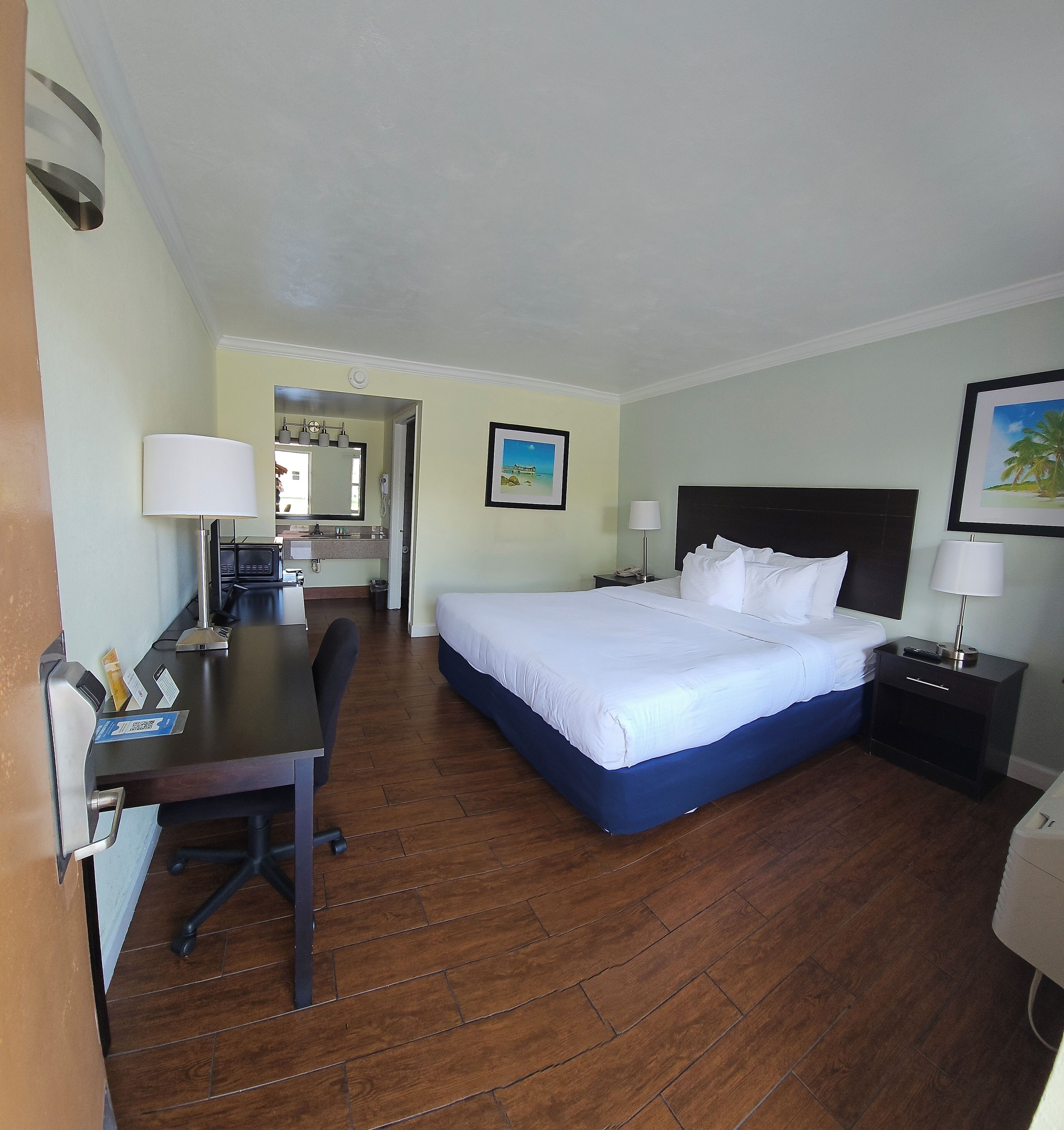 Une chambre d’hôtel avec un lit, un bureau, une chaise et une salle de bain visible au fond.