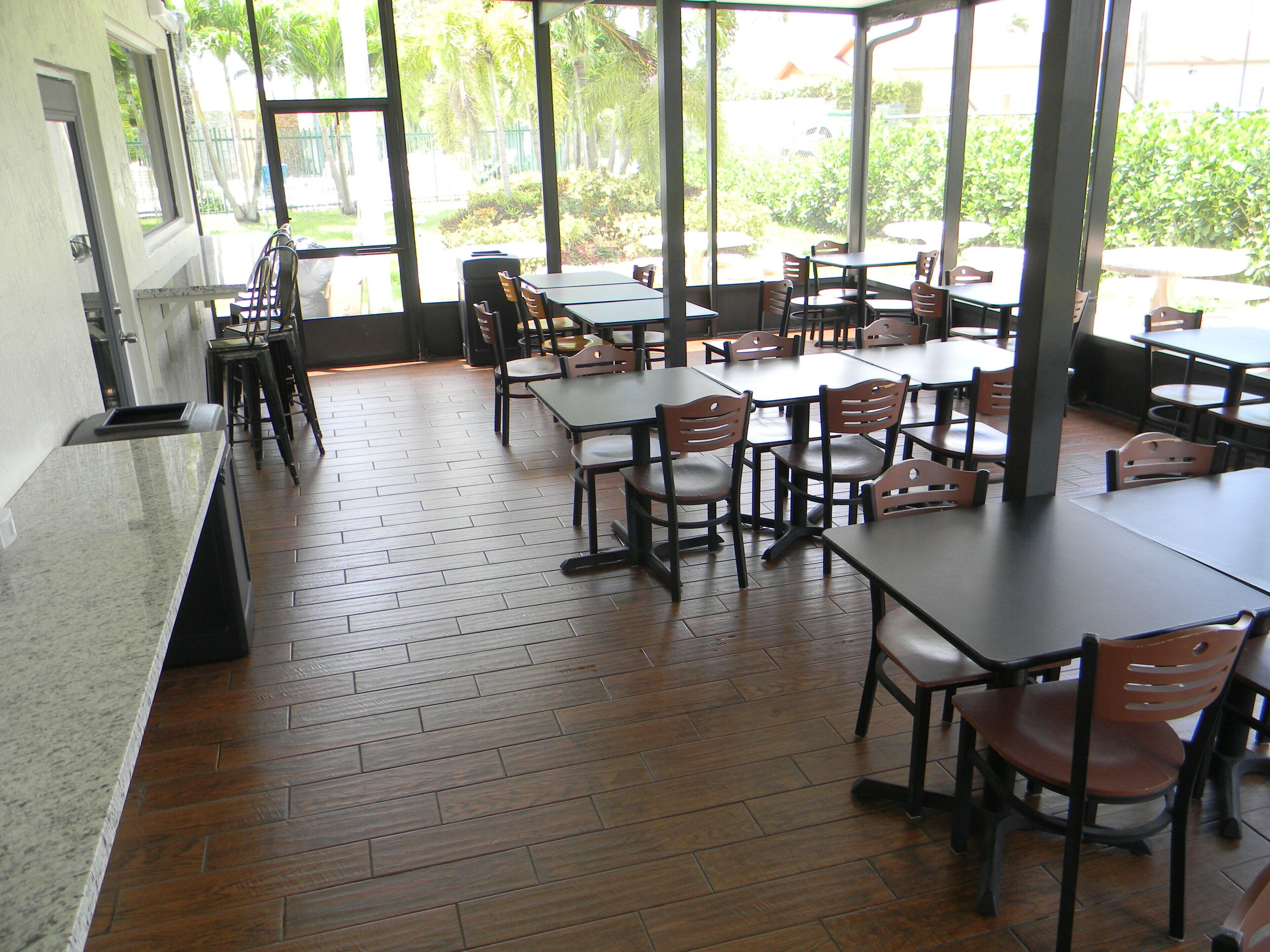 A restaurant with wooden flooring, multiple tables and chairs, and large windows offering a view of greenery outside.