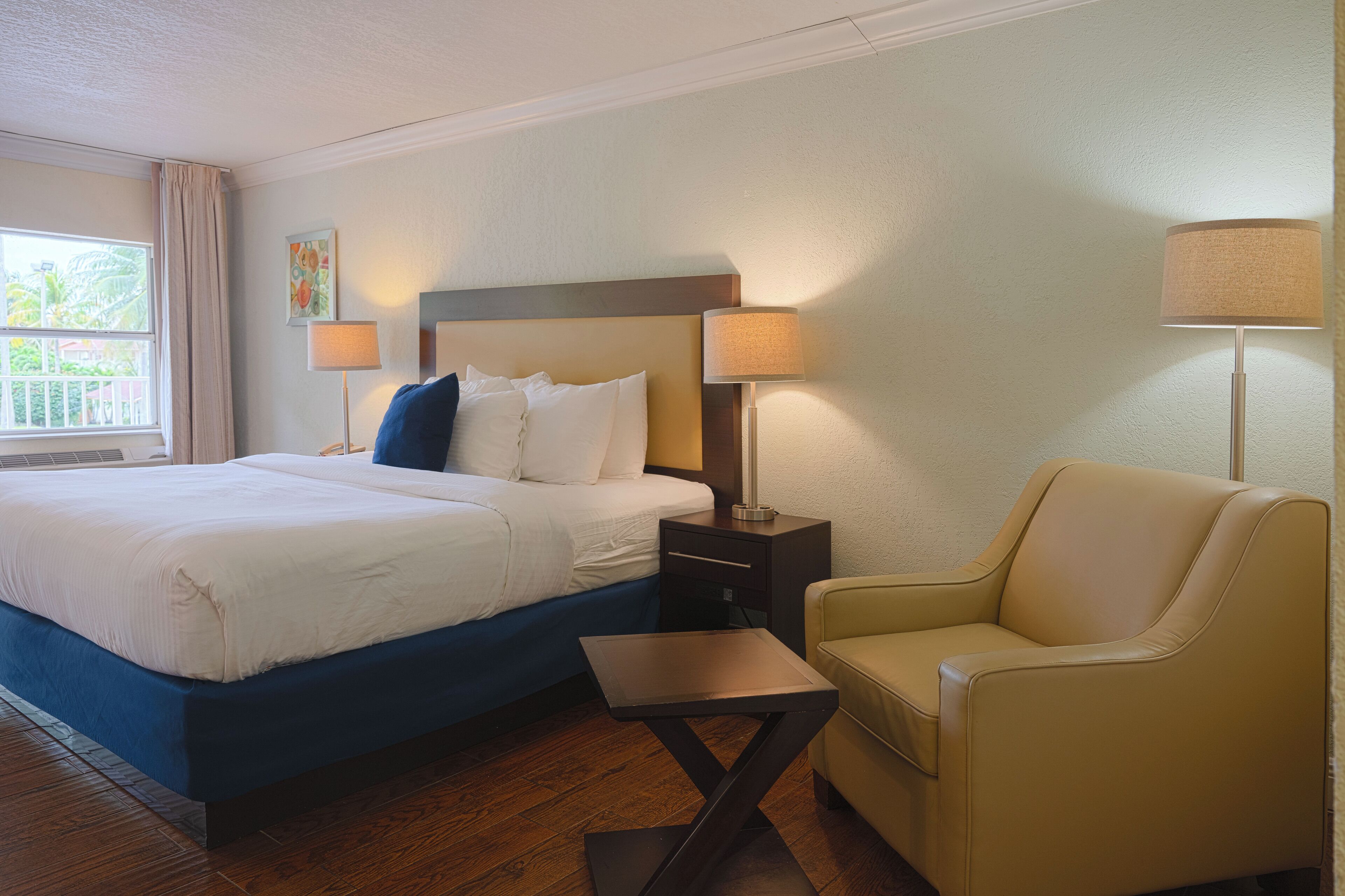A hotel room with a bed, bedside lamps, a chair, and a small table.