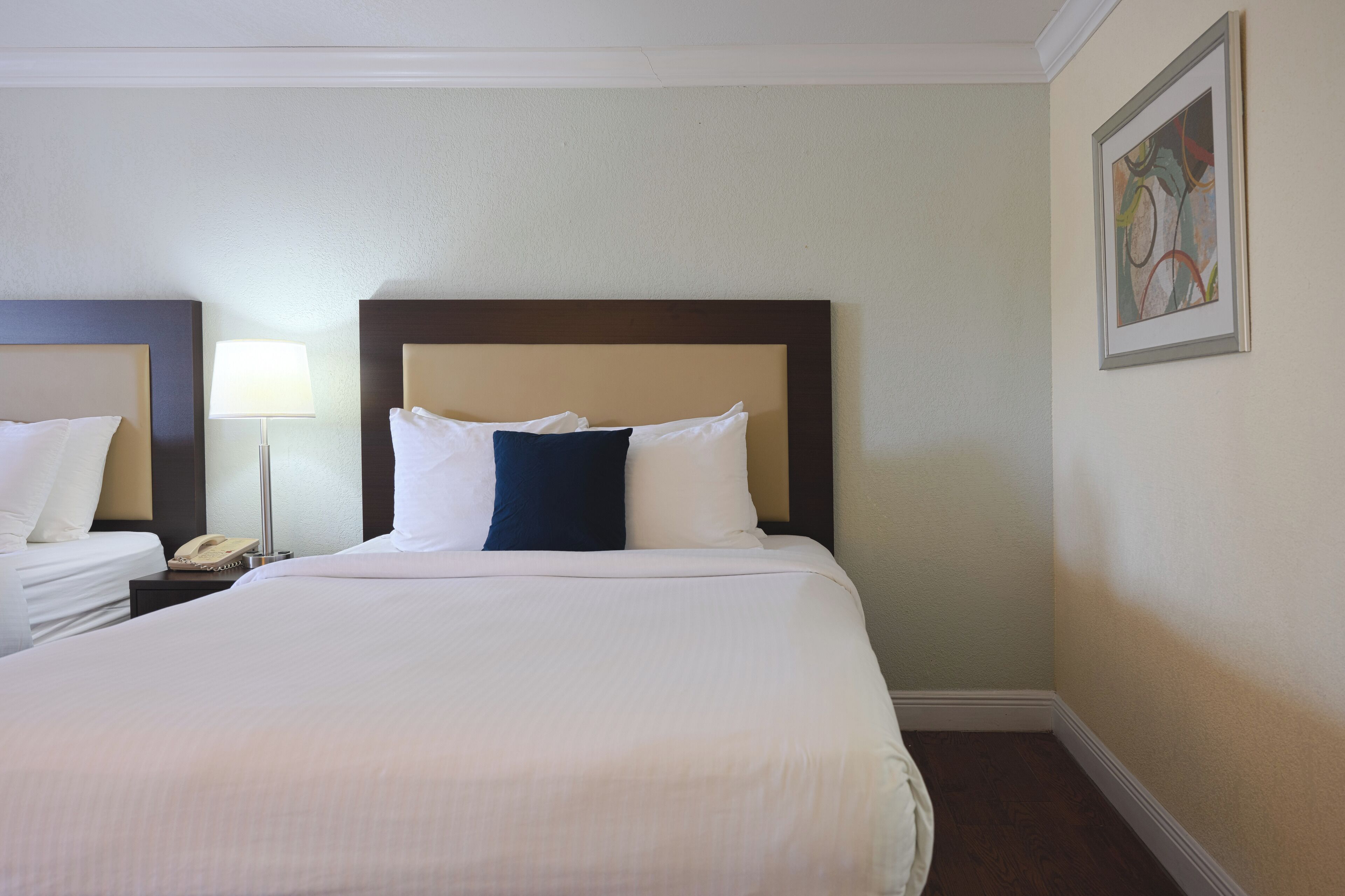 Een hotelkamer met een groot bed, een bedlampje, een telefoon en een lijst met een kunstwerk aan de muur.