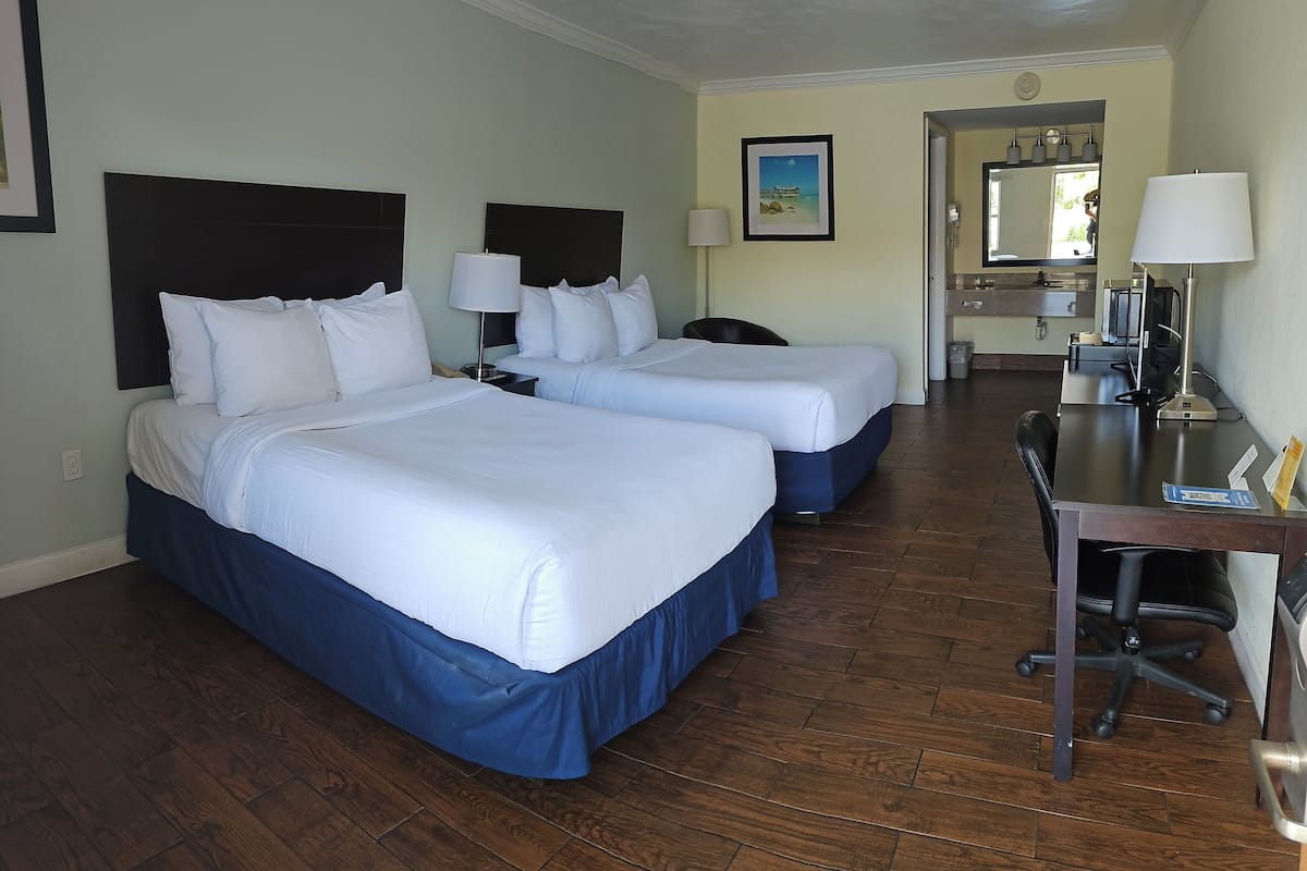 Une chambre d’hôtel avec deux lits, un bureau et une salle de bain que l’on aperçoit à l’arrière-plan.