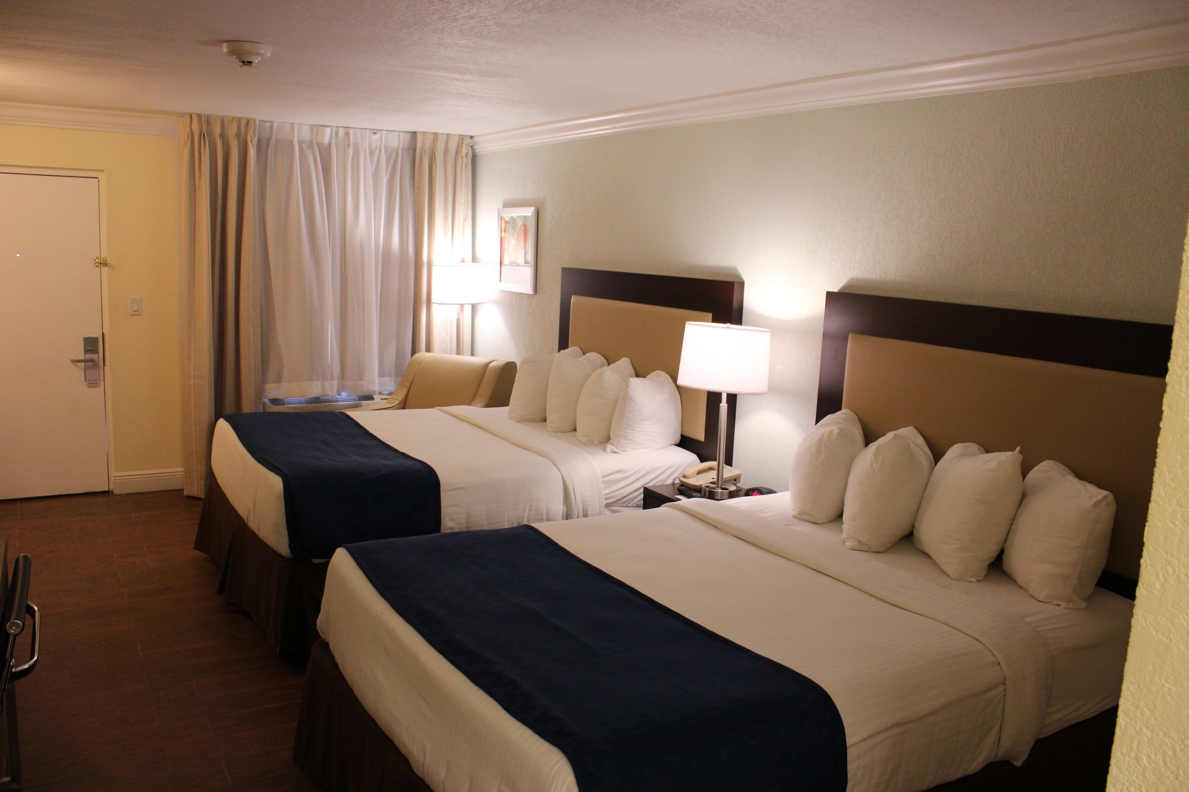 A hotel room with two beds, a nightstand with a lamp, and a door.