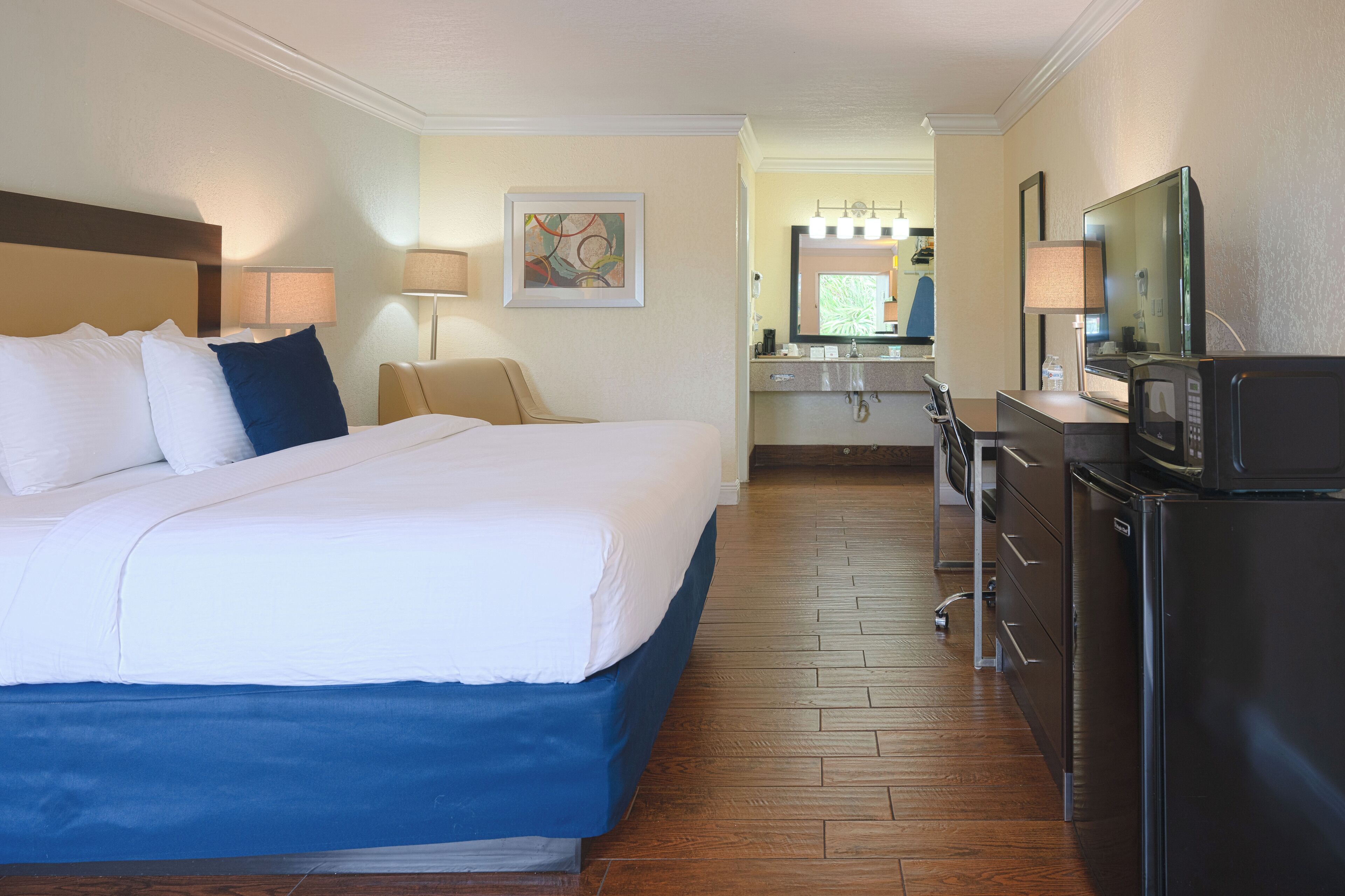 A hotel room with a large bed, a desk with a chair, a refrigerator, and a microwave.