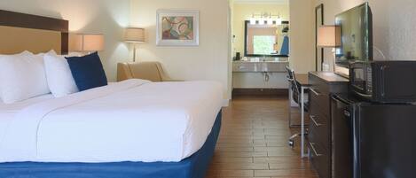 A hotel room with a large bed, a desk with a chair, a refrigerator, and a microwave.