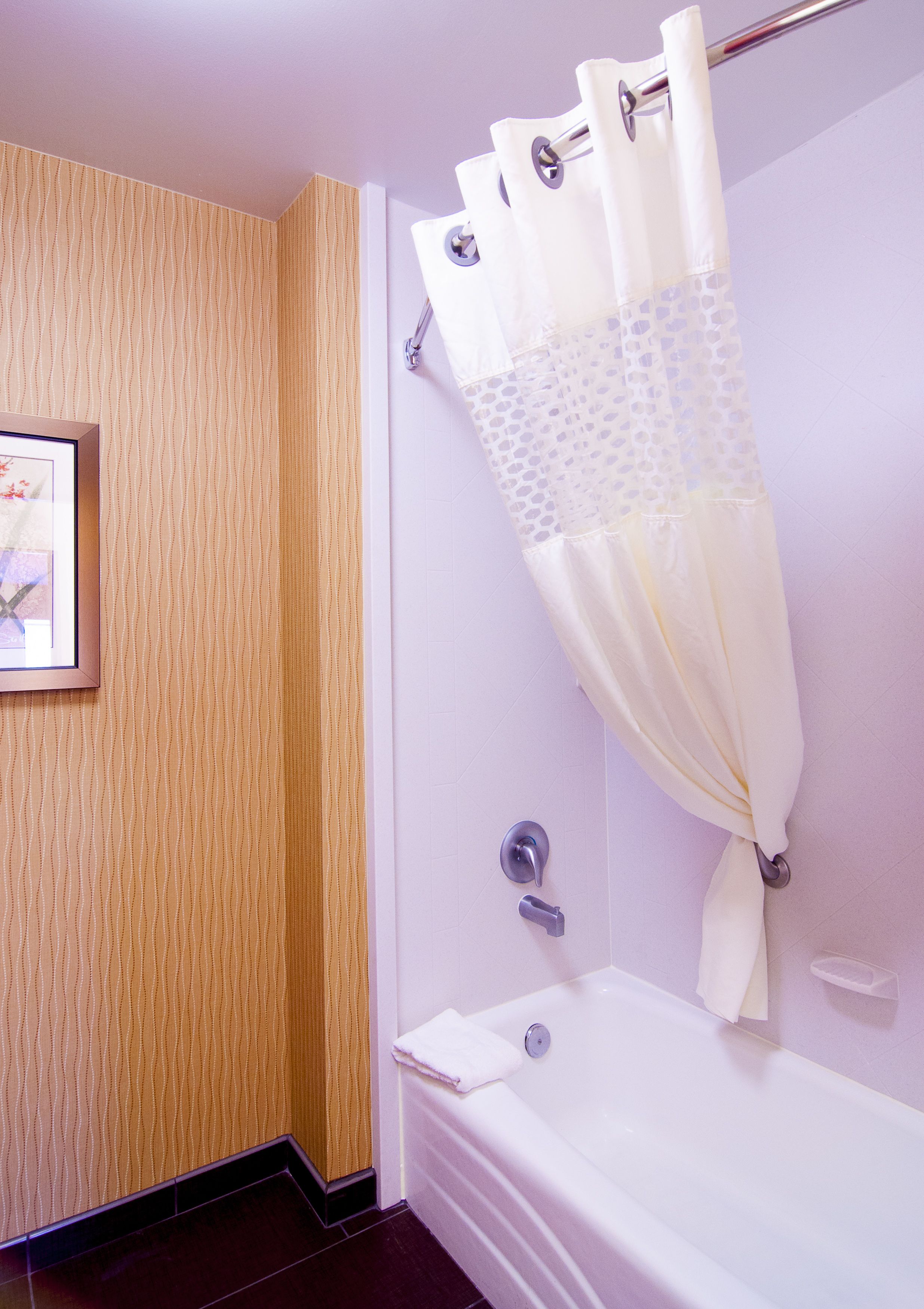 A bathroom with a bathtub, a shower curtain, and a framed picture on the wall.