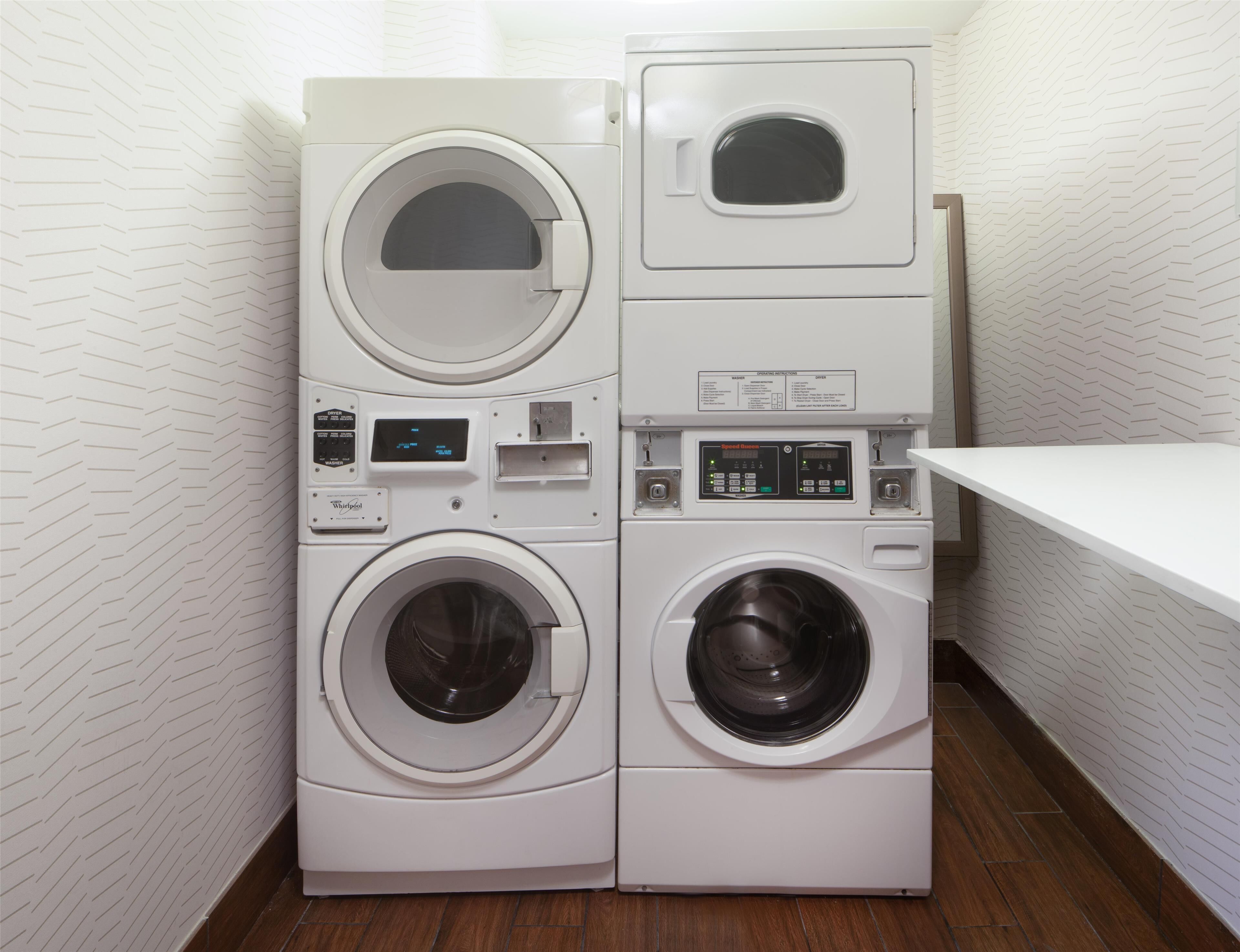 A compact laundry area with two stacked washing machines and a dryer, featuring control panels and a small shelf.