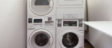 A compact laundry area with two stacked washing machines and a dryer, featuring control panels and a small shelf.