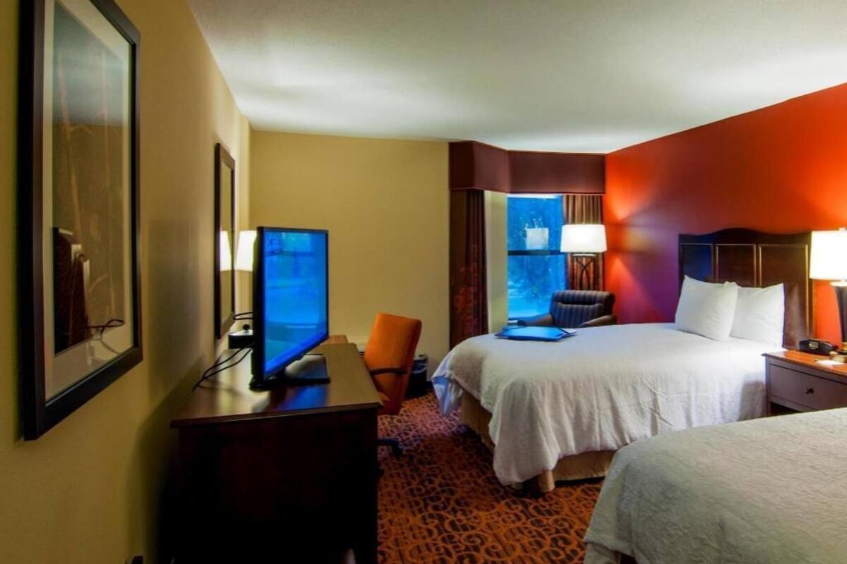 A hotel room with a bed, a desk with a computer, a chair, and a window.