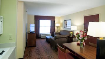 Habitación de hotel con cama, escritorio, computadora, silla, mesa y lámpara.
