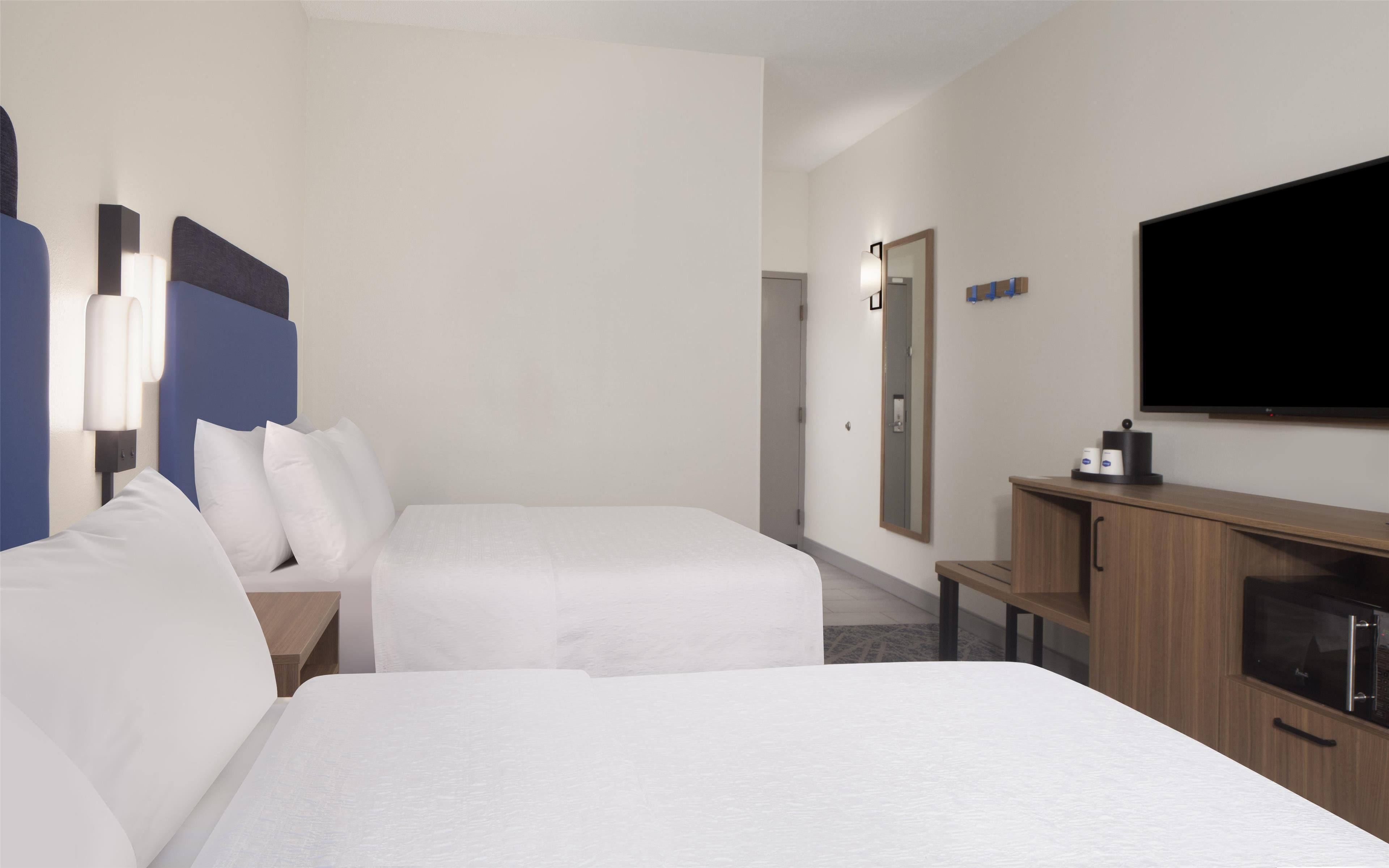 A hotel room with two beds, a TV, a microwave, and a small cabinet.