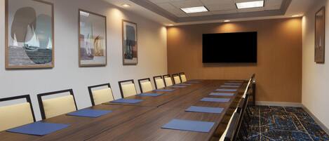 A conference room with a long table, chairs, a flat-screen TV, and framed artwork on the walls.