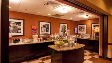 Uma cozinha de hotel com piso xadrez, bancadas de granito e diversos eletrodomésticos.