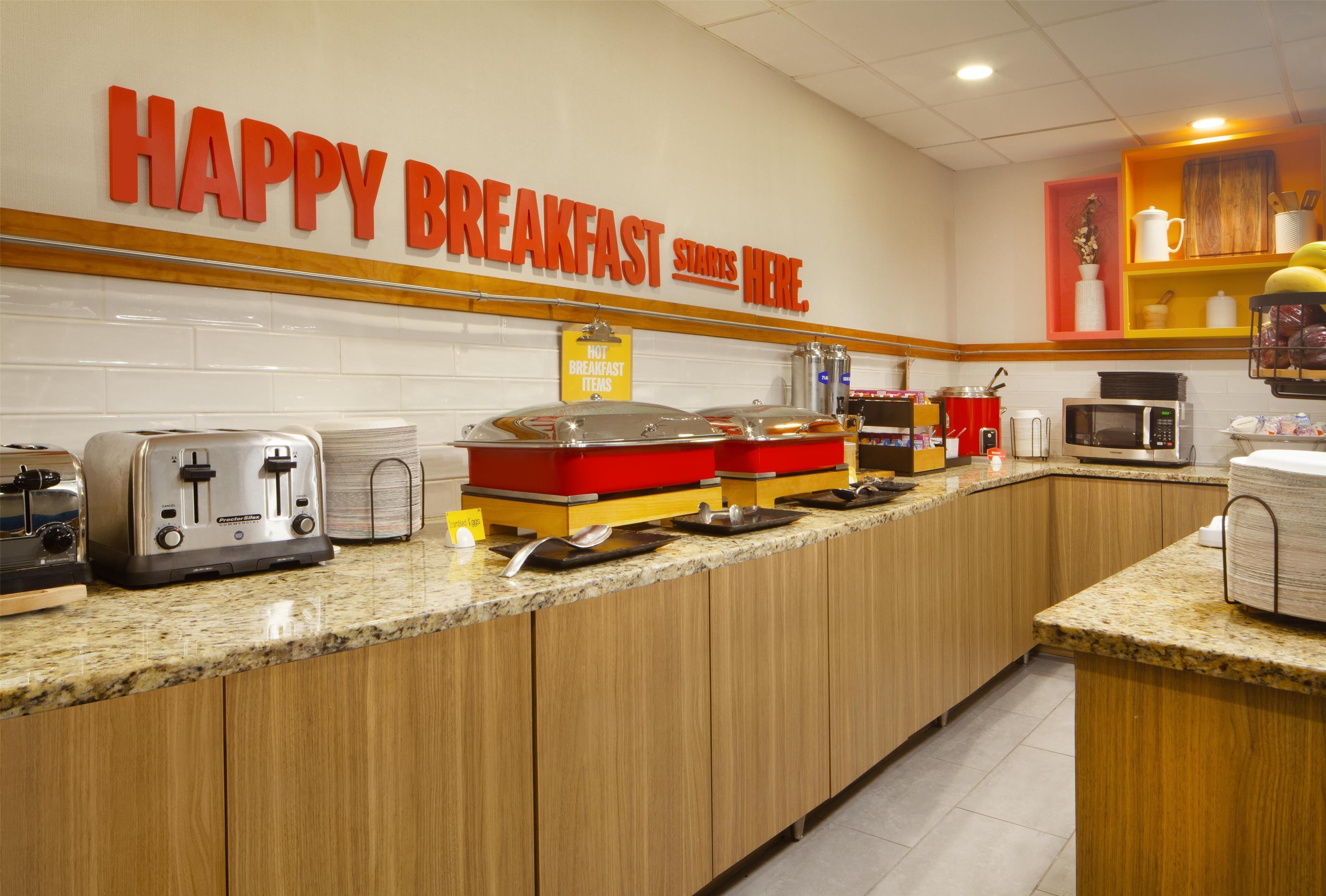 A breakfast bar with toasters, a microwave, and a sign that reads "HAPPY BREAKFAST STARTS HERE."