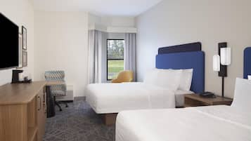 Une chambre d’hôtel avec deux lits, un bureau, une chaise, une télévision et une fenêtre avec des rideaux.