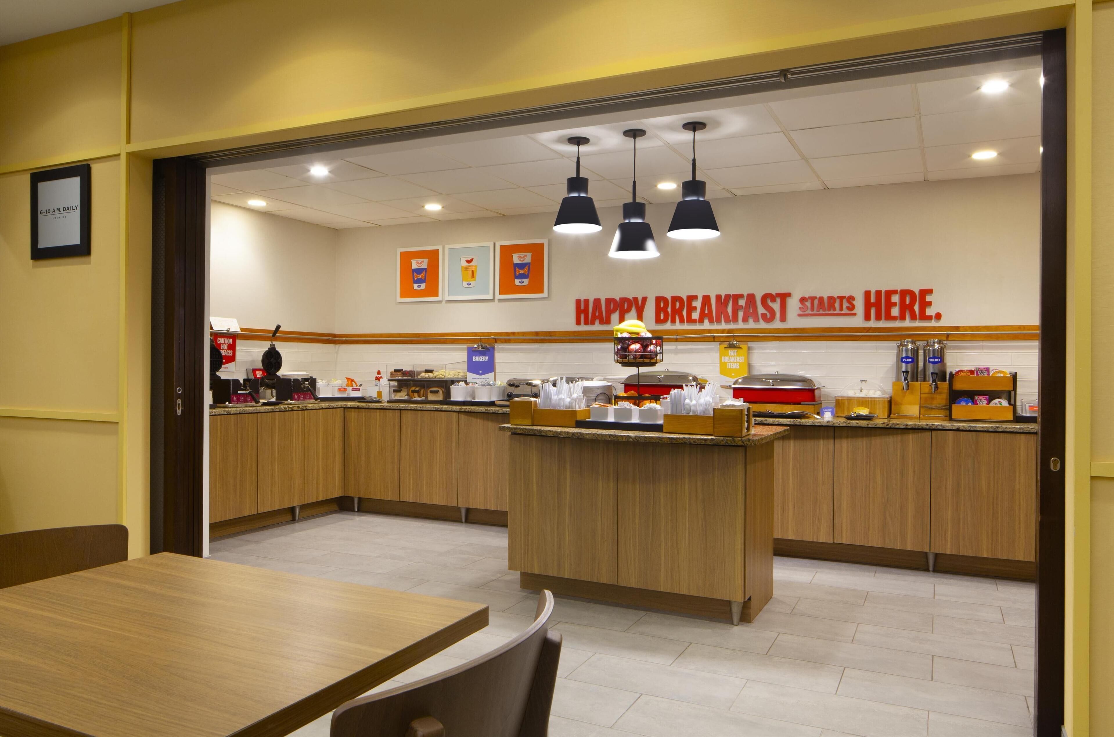 Un área de desayuno con armarios de madera, una isla central con alimentos y un letrero que dice "HAPPY BREAKFAST STARTS HERE".