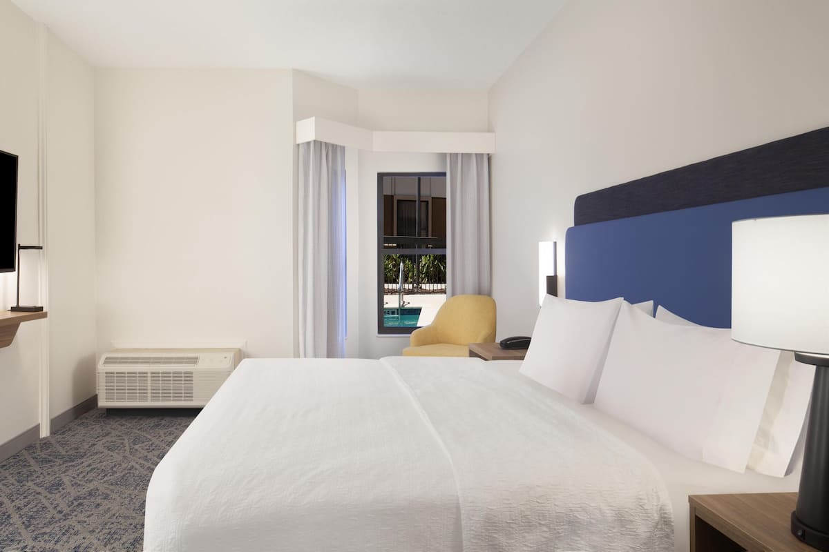 A hotel room with a large bed, a TV, a desk, and a view of a swimming pool.