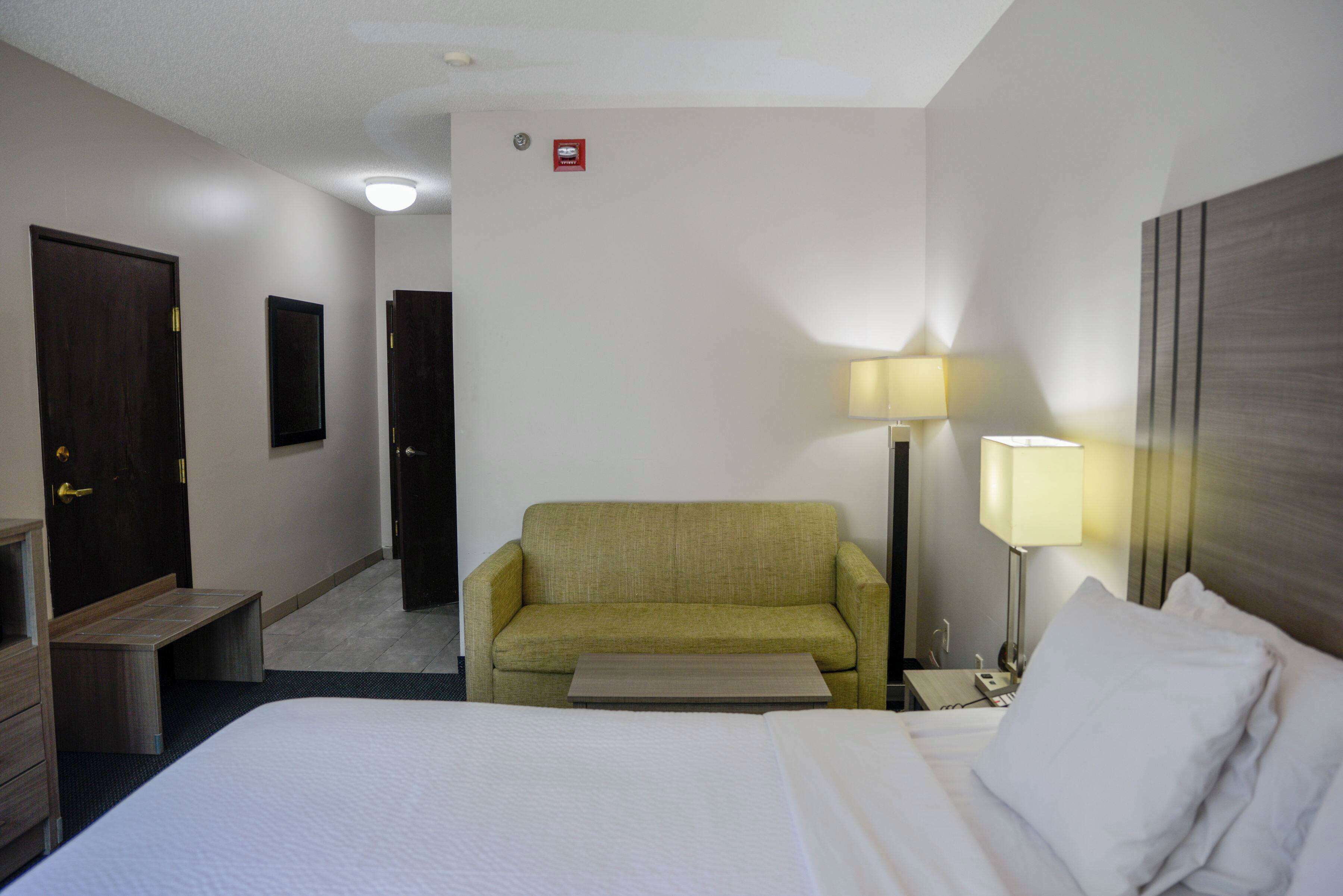 A hotel room with a bed, a sofa, a desk, a lamp, and a door.