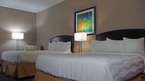 Ein Hotelzimmer mit zwei Betten, jeweils mit Kopfteil, Nachttischlampen und einem gerahmten abstrakten Gemälde an der Wand.