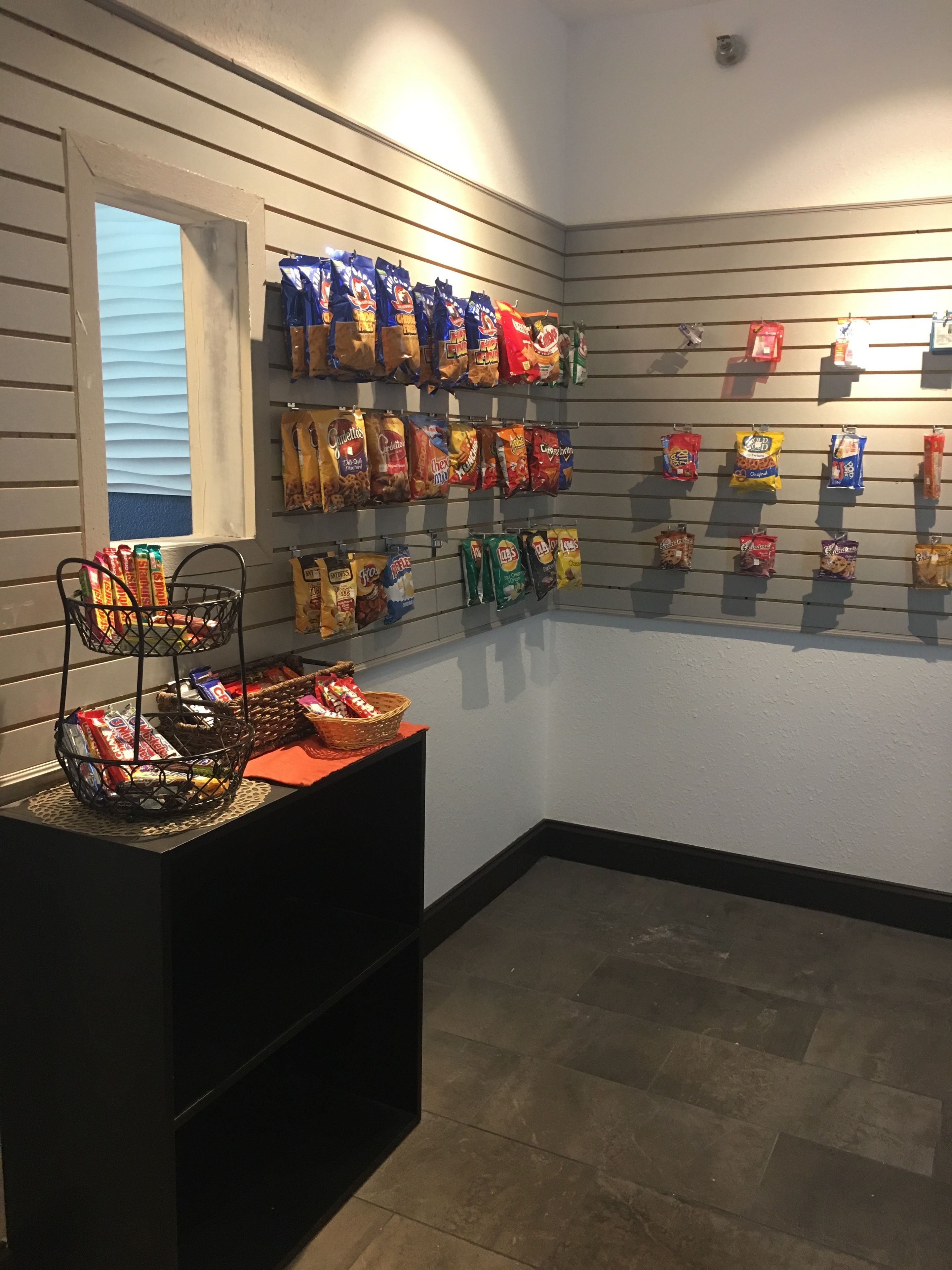 Exposição de petiscos com diversos lanches embalados pendurados na parede e uma cesta de petiscos sobre uma mesa.