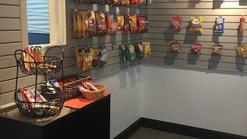 Exposição de petiscos com diversos lanches embalados pendurados na parede e uma cesta de petiscos sobre uma mesa.