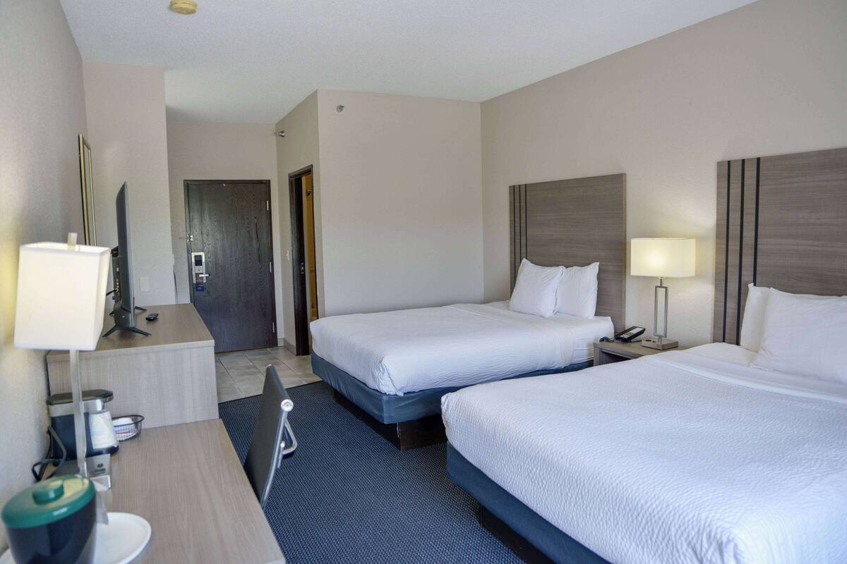 Hotellihuone, jossa on kaksi sänkyä, kirjoituspöytä lampun kanssa, televisio ja minibaari.