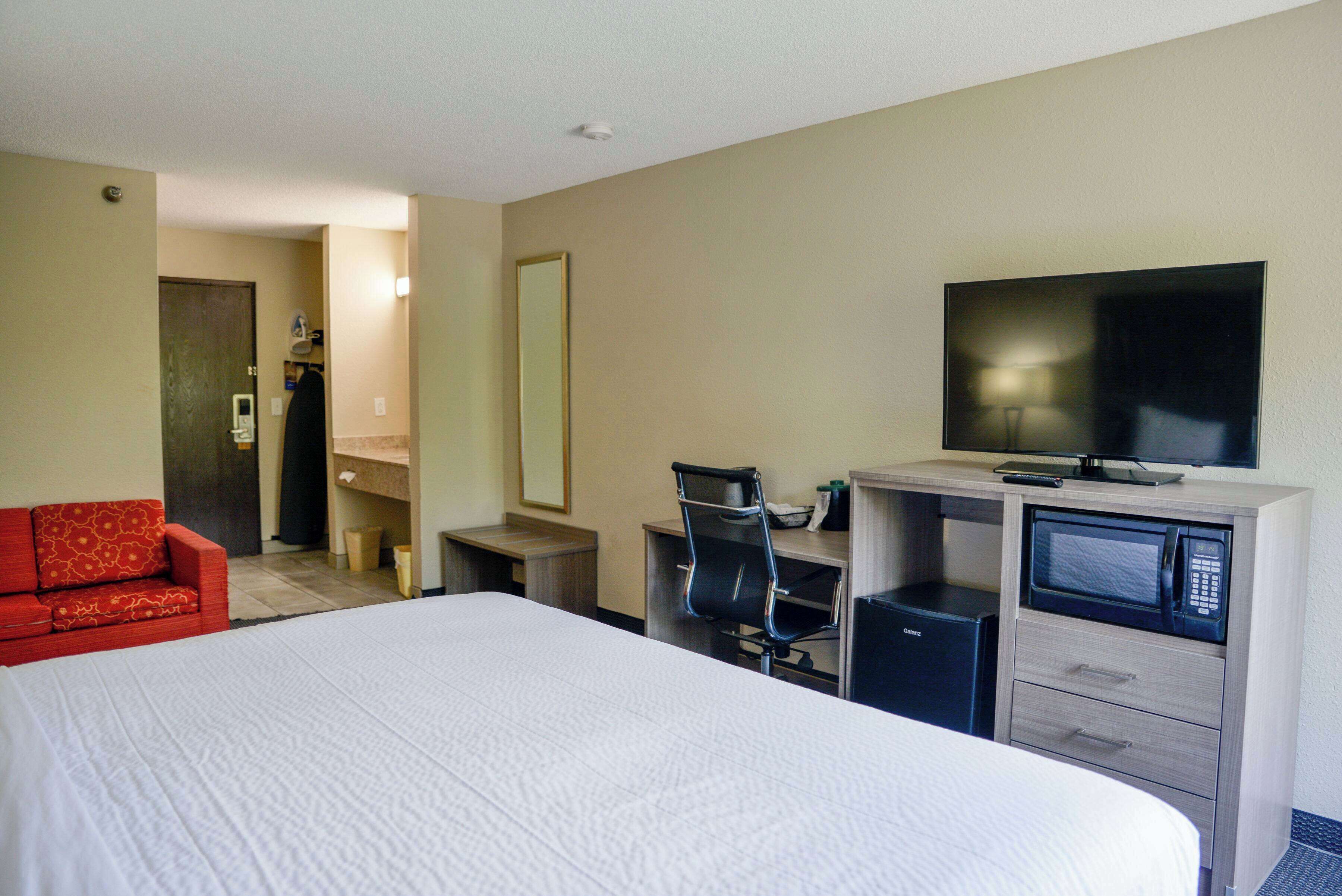 A hotel room with a large bed, a red sofa, a desk with a computer, a microwave, and a TV.