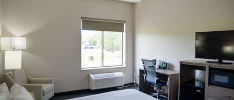 Una habitación de hotel con una cama, un escritorio, una silla, un televisor y una ventana con persianas.