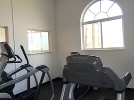 A gym with treadmills and a stationary bike, a window with a view of the outside, and a door to the left.