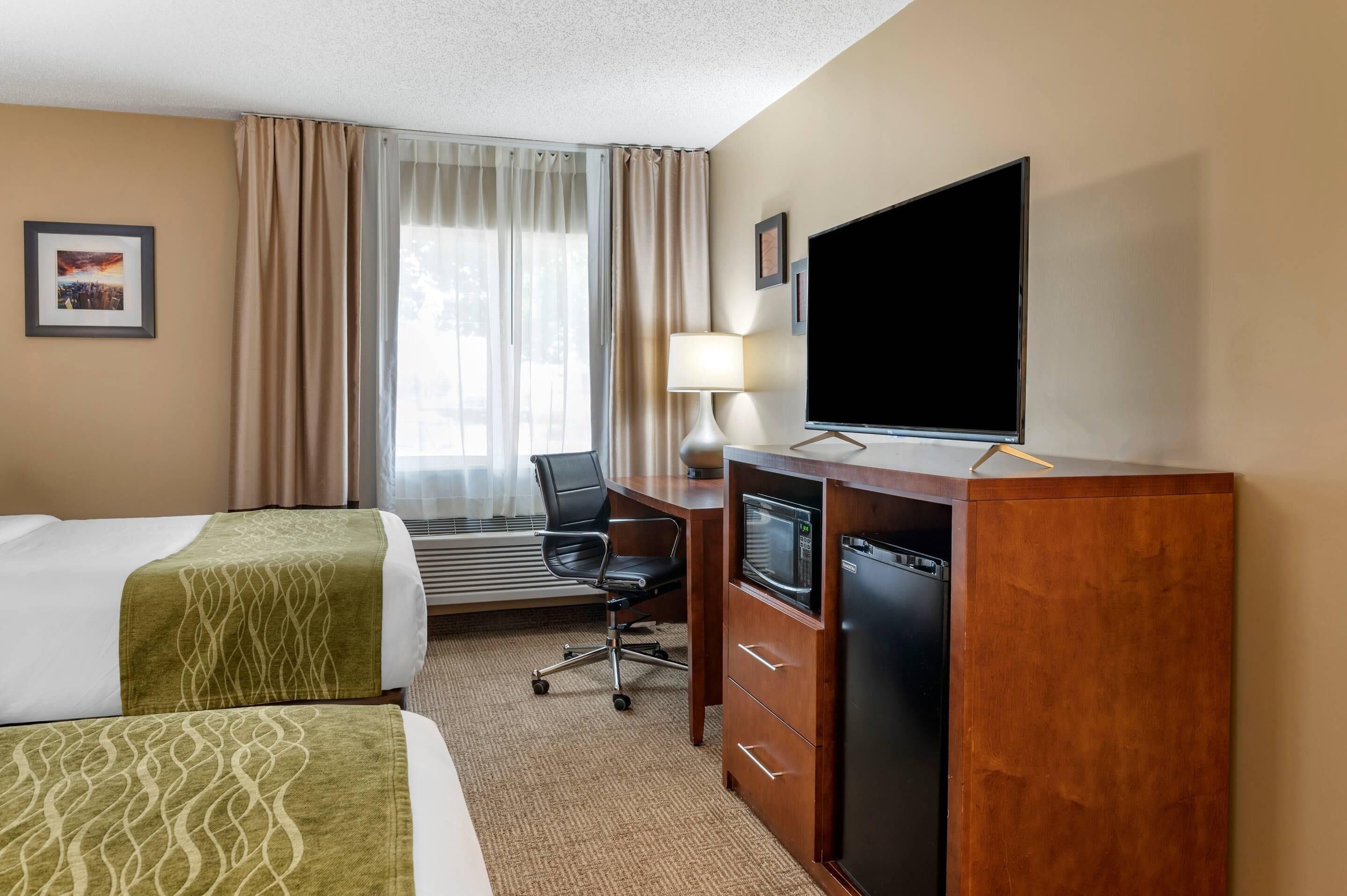 A hotel room with two beds, a desk with a television, a microwave, and a refrigerator.