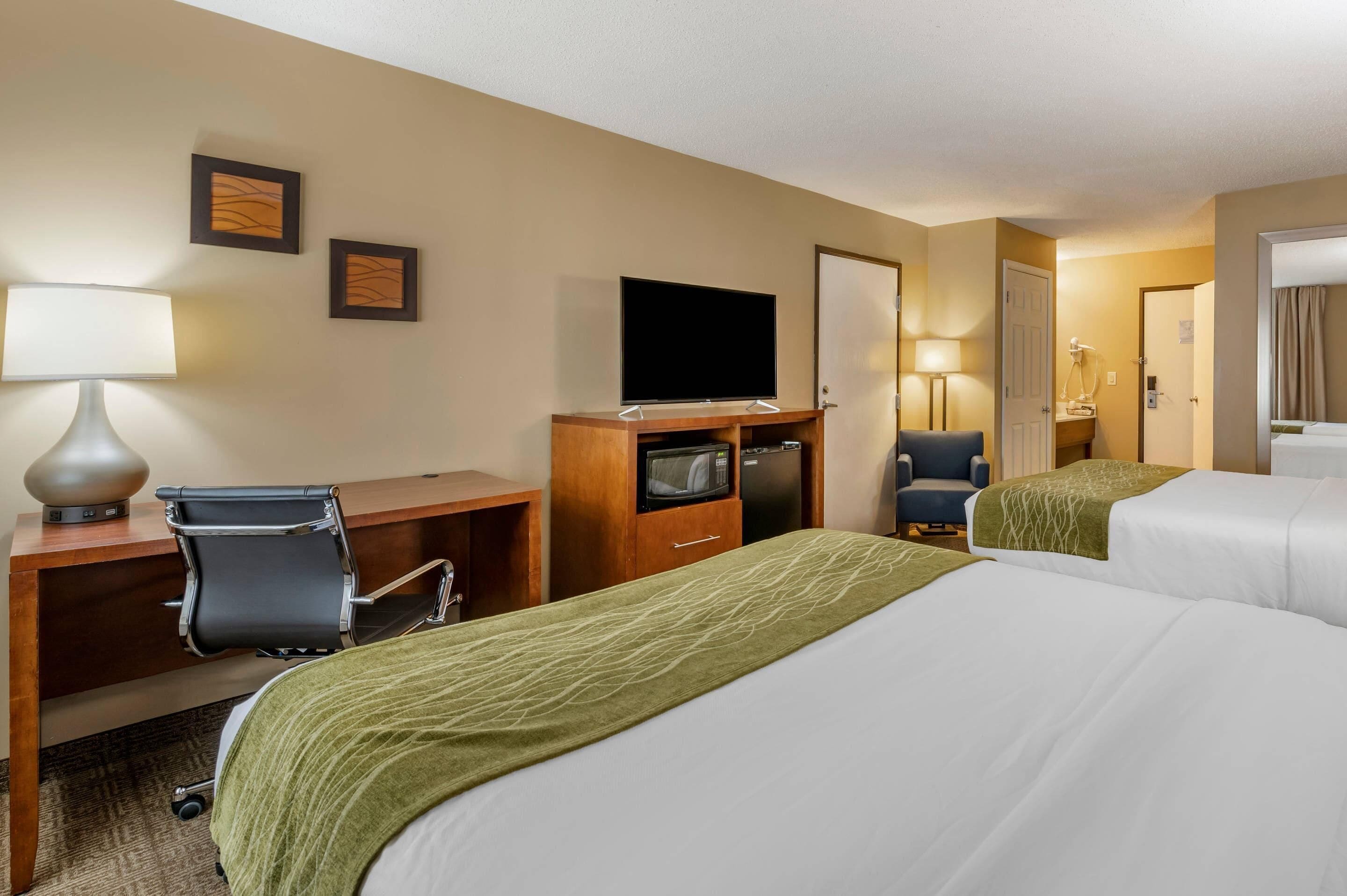 A hotel room with two beds, a desk with a chair, a television, a microwave, and a door.