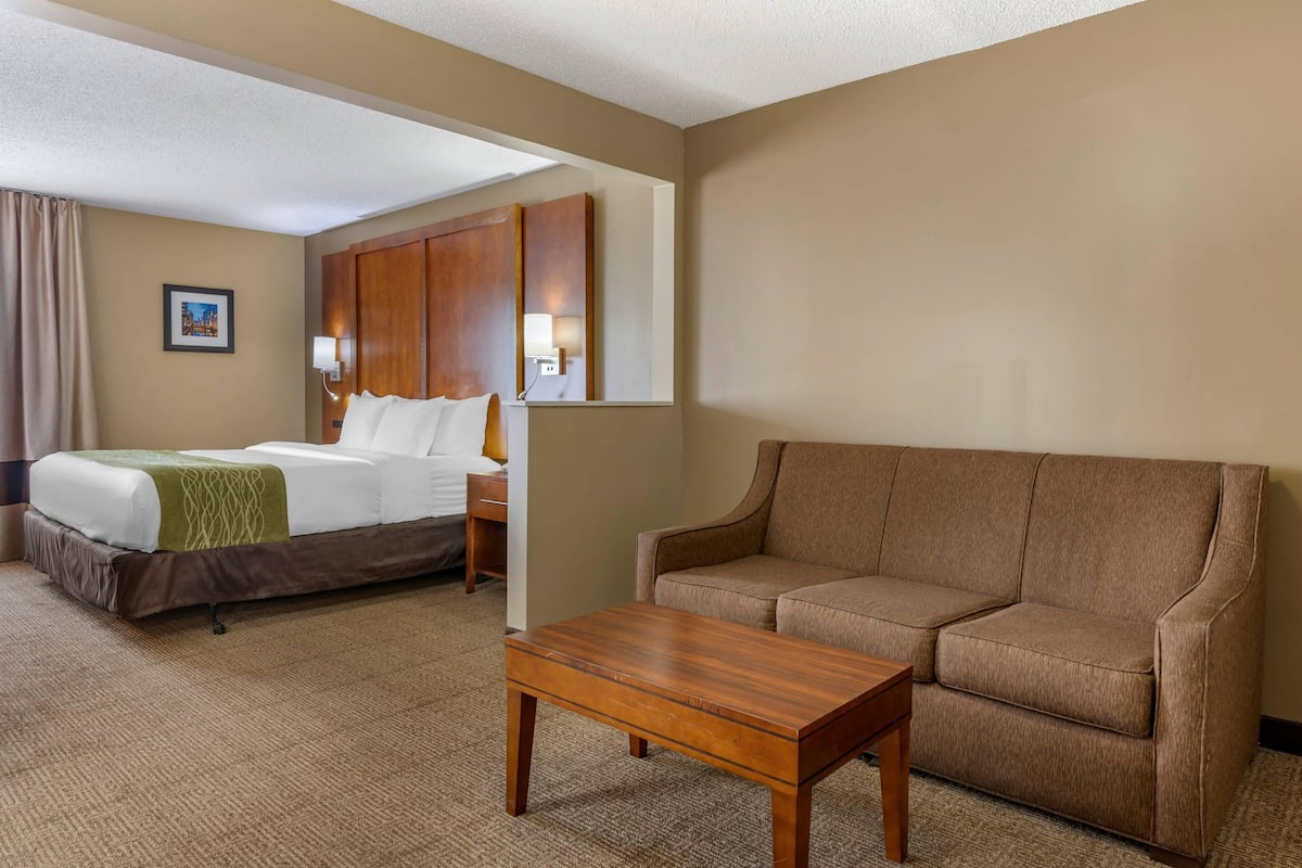 A hotel room with a bed, a sofa, a wooden coffee table, and a wall-mounted TV.