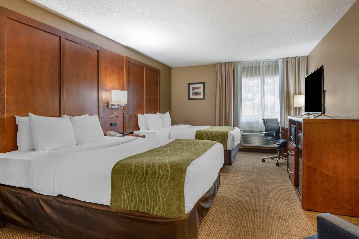 A hotel room with two beds, a desk, a TV, and a window with curtains.