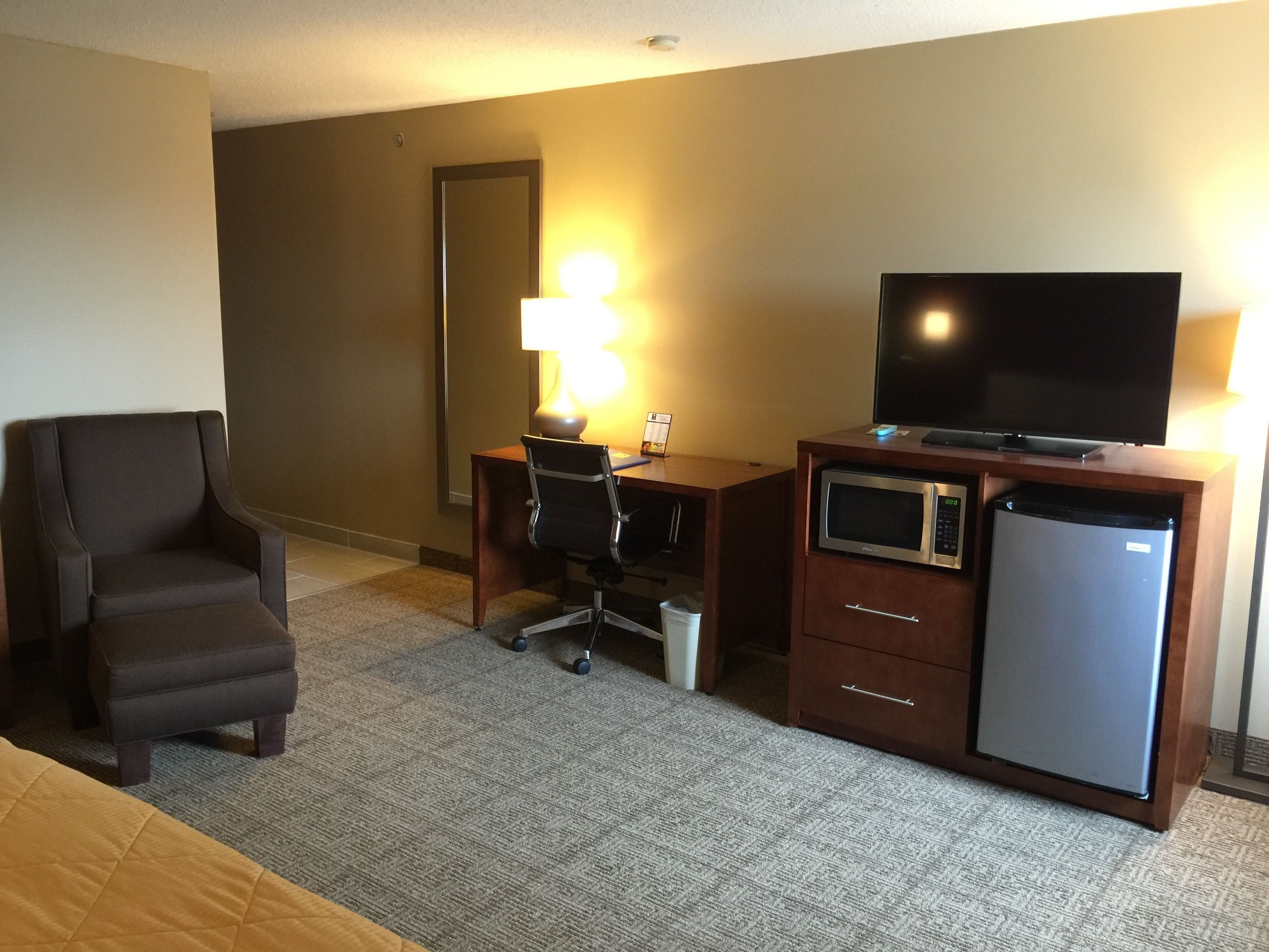 A hotel room with a desk, chair, television, microwave, and refrigerator.