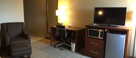 A hotel room with a desk, chair, television, microwave, and refrigerator.
