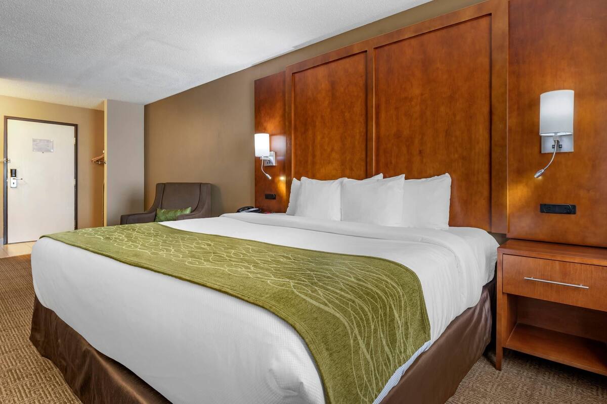 A hotel room with a large bed, a wooden headboard, a nightstand, and a chair.