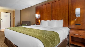 Una habitación de hotel con una cama grande, cabecera de madera, mesita de noche y una silla.