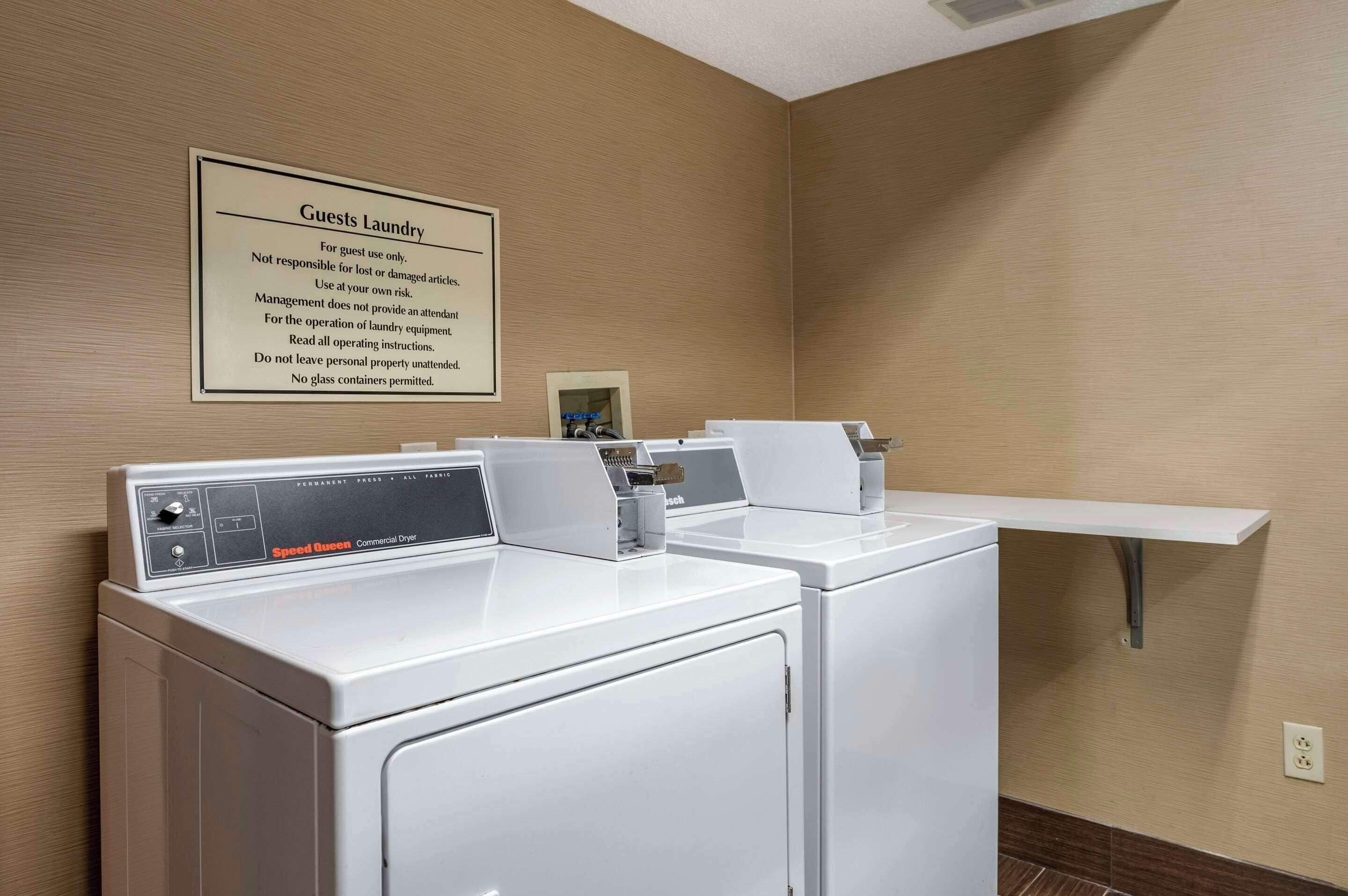 A hotel laundry room with two Speed Queen commercial dryers and a sign detailing guest laundry rules.