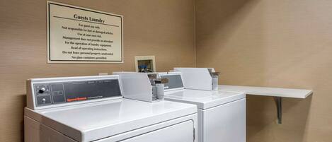 A hotel laundry room with two Speed Queen commercial dryers and a sign detailing guest laundry rules.