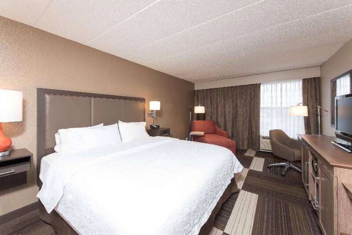 A hotel room with a bed, a desk, a chair, and a television.