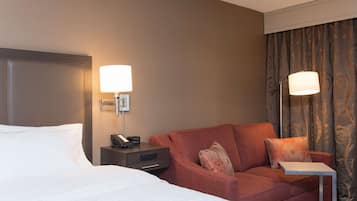 Een hotelkamer met een bed, een sofa, een nachtkastje met lamp en een klein tafeltje.