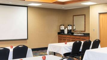 Una sala de conferencias con mesas, sillas, una pantalla para proyector y un rincón para café.